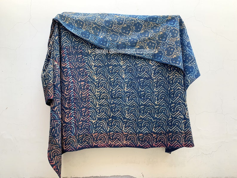 May include: A blue and white kantha quilt with a geometric pattern. The quilt is folded in half and hanging from a hook.
