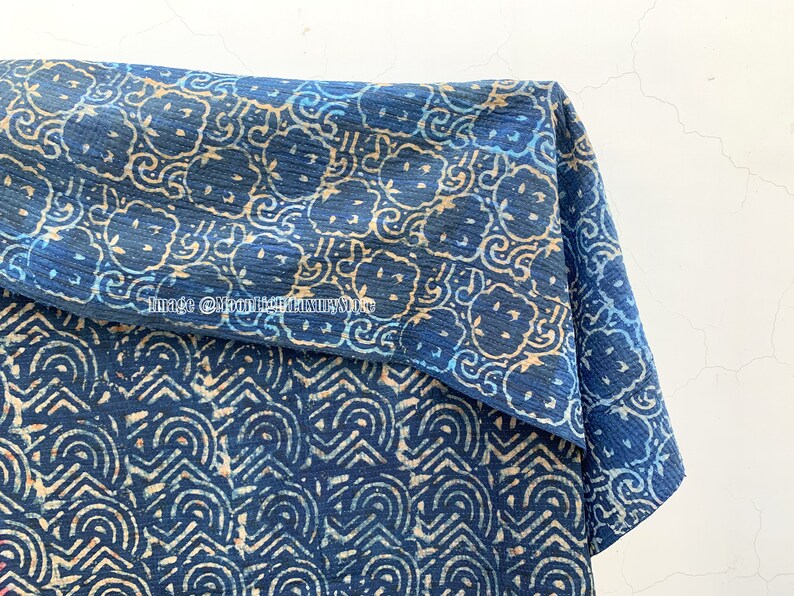 May include: A blue and white cotton fabric with a repeating pattern of stylized flowers and swirls. The fabric is folded in half, showing both sides of the pattern.
