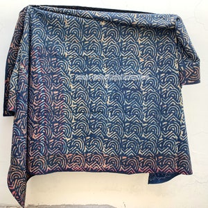 May include: A blue and white kantha quilt with a geometric pattern. The quilt is folded and hanging on a white wall.