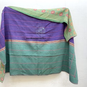 May include: A purple and green kantha quilt with a floral pattern. The quilt is folded and hanging on a white wall.