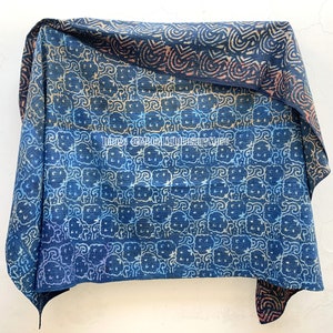 May include: A blue and white kantha quilt with a repeating pattern of stylized flowers. The quilt is folded in half and has a brown and orange border.