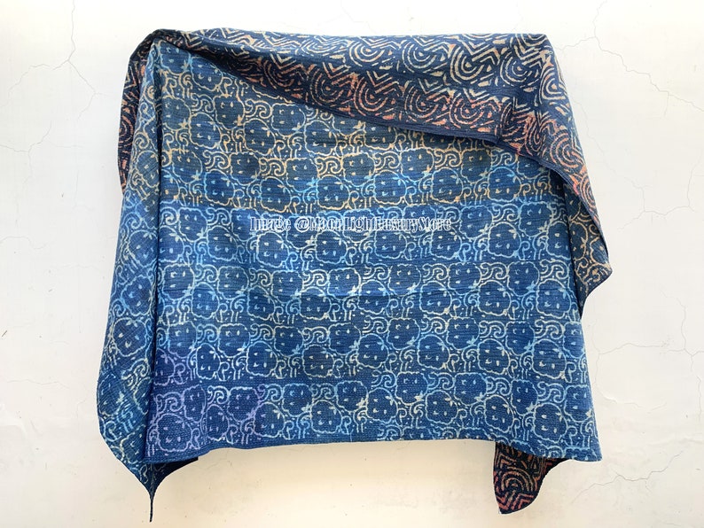 May include: A blue and white kantha quilt with a repeating pattern of stylized flowers. The quilt is folded in half and has a brown and orange border.