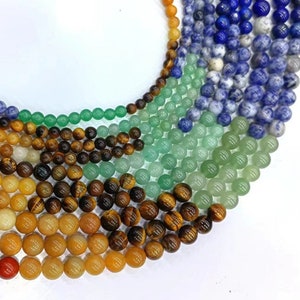 Puede incluir: Una colección de cuentas redondas de piedras preciosas en varios colores, incluyendo rojo, naranja, amarillo, verde, azul y marrón. Las cuentas están dispuestas en un patrón circular, con las cuentas más grandes en el centro y las cuentas más pequeñas en el exterior.