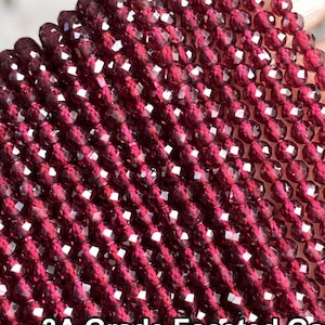 Puede incluir: Una hebra de cuentas de granate facetadas de grado 3A. Las cuentas son de color rojo intenso y tienen un alto pulido. El texto "3A Grade Faceted Garnet 特级石榴石刻面" es visible en la imagen.