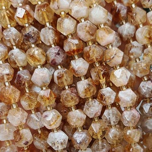 May include: A collection of citrine gemstone beads in shades of yellow, orange, and brown. The beads are faceted and strung together with gold-coloured connectors. The gemstones have a geometric shape, creating a shimmering effect.