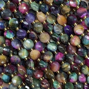 May include: A collection of faceted gemstone beads in shades of purple, green, brown, and gold. The beads are strung on gold-coloured string, creating a shimmering effect. The beads are held in a hand.