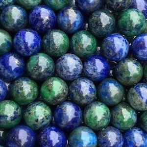 Peut inclure: Un ensemble de perles rondes dans des tons de bleu profond et de vert. Les perles sont enfilées ensemble, créant un affichage texturé et coloré. Les perles ont une finition polie et brillante.