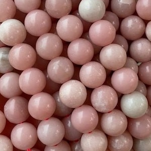 Peut inclure: Un brin de perles rondes de pierres précieuses roses et blanches. Les perles sont lisses et polies, et ont un aspect naturel et organique.