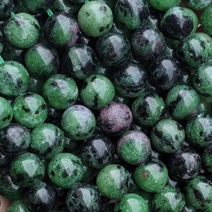 May include: A strand of green and black gemstone beads. The beads are round and have a speckled appearance.