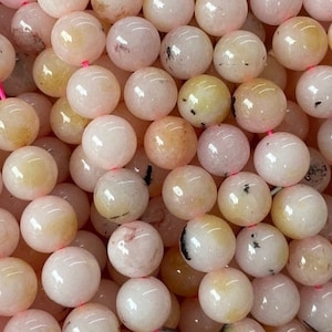 May include: A strand of round, pink and yellow gemstone beads with black inclusions. The beads are smooth and polished.