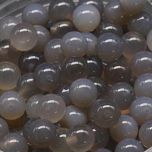 May include: A bowl of grey agate beads. The beads are round and smooth, and they have a slightly translucent appearance.