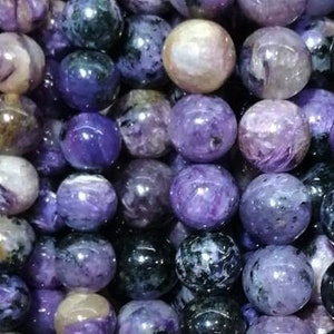 Puede incluir: Una hebra de cuentas redondas de piedras preciosas de color púrpura y negro. Las cuentas tienen un patrón veteado y en espiral.
