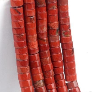 Peut inclure: Brins de perles de jaspe rouge. Les perles sont cylindriques avec une surface plate et un trou au centre. Les perles sont de couleur brun rougeâtre avec quelques taches brun foncé. Les perles sont enfilées sur une ficelle blanche.