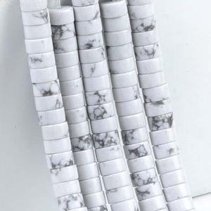 May include: Strands of white and gray marbled beads. The beads are flat, disc-shaped, and strung together. The beads are made of a stone-like material and are suitable for jewelry making. The beads are a neutral color and can be used in a variety of designs.