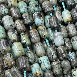May include: A strand of turquoise gemstone beads, each bead is a dark green and blue colour with a mottled pattern. The beads are oval shaped and have a smooth, polished finish.