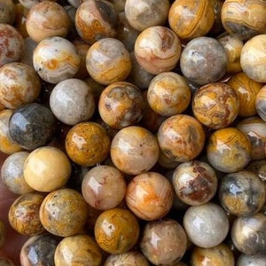 May include: A close-up of a strand of round, brown, yellow, and gray agate beads. The beads have a natural, polished finish and are perfect for jewelry making.