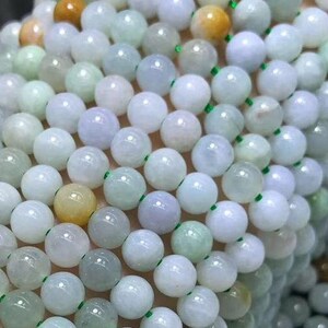 Puede incluir: Primer plano de m&uacute;ltiples hilos de cuentas redondas y pulidas. Las cuentas son principalmente blancas y verde p&aacute;lido, con acentos amarillos y naranjas ocasionales. Las cuentas est&aacute;n ensartadas en un fino cord&oacute;n verde, creando una apariencia delicada y elegante. El tema general es la joyer&iacute;a.