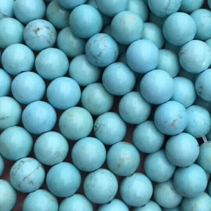 May include: A strand of turquoise blue round beads. The beads are smooth and polished, and they have a natural, slightly mottled appearance.