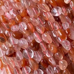 Könnte beinhalten: Eine Strähne aus durchscheinenden, hellrosa und orangefarbenen Edelsteinperlen. Die Perlen sind oval geformt und haben eine glatte, polierte Oberfläche.