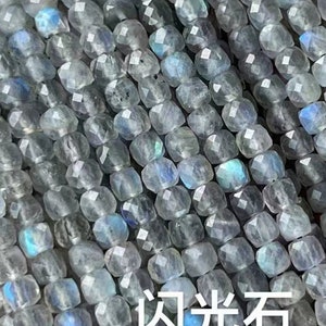 May include: A strand of gray labradorite gemstone beads. The beads are faceted and have a shimmery, iridescent quality. The text "闪光石 Labradorite" is visible in the image.