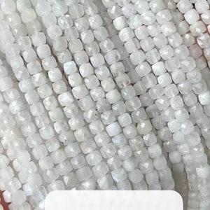 May include: A strand of white moonstone beads, faceted and square shaped. The beads are strung on a clear thread and are approximately 4mm in size. The strand is labeled "Moonstone".