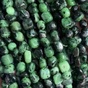 May include: A collection of gemstone beads in shades of green and black. The beads have a mix of shapes, with a speckled appearance. The beads are strung together, creating a textured and colourful display. The gemstones are held in a hand.