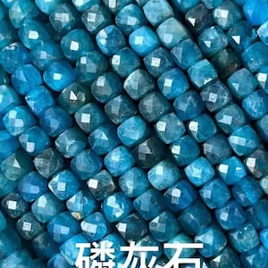 Puede incluir: Primer plano de una hebra de cuentas de apatita azul. Las cuentas son facetadas y tienen forma cuadrada. El texto "Apatite" está escrito en letras blancas sobre fondo negro.