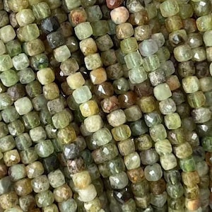 May include: A strand of green and brown faceted gemstone beads. The beads are small and square-shaped, and they are strung on a clear thread.
