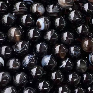 May include: A strand of black agate beads with white and grey banding. The beads are round and smooth, and they are strung on a clear thread.