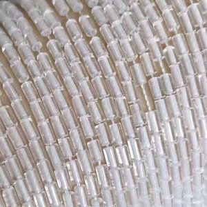May include: A close-up of a strand of iridescent white glass beads. The beads are small and cylindrical, and they are strung together on a clear thread. The beads have a subtle shimmer and sparkle.