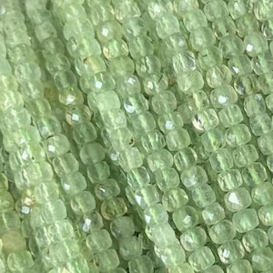 Op de afbeelding: Een streng lichtgroene edelsteen kralen, elke kraal is gefacetteerd en heeft een vierkante vorm.