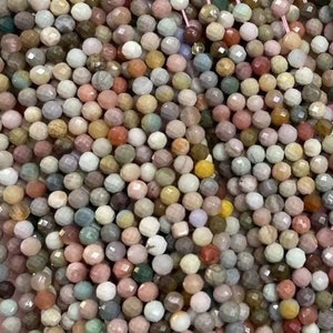 Puede incluir: Una hebra de cuentas de piedras preciosas multicolores. Las cuentas son pequeñas y redondas, con un acabado facetado. Los colores son una mezcla de rosa, marrón, verde y blanco.