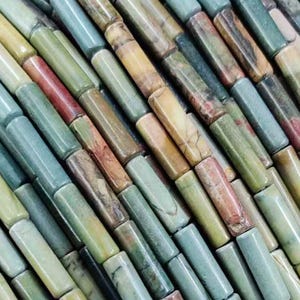 Puede incluir: Una hebra de cuentas de piedras preciosas multicolores. Las cuentas son cilíndricas y tienen un patrón moteado de verde, marrón, amarillo y rojo.