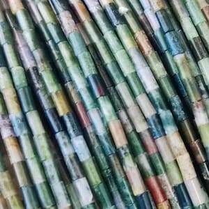 Op de afbeelding: Een streng groene, bruine en witte edelsteen kralen. De kralen zijn klein en cilindrisch en zijn aan elkaar geregen op een doorzichtige draad.