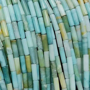 Puede incluir: Una hebra de cuentas de piedras preciosas de color azul turquesa y verde, cada cuenta es un cilindro largo y delgado.