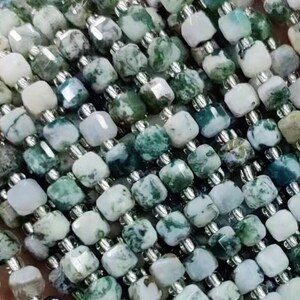 Puede incluir: Una hebra de cuentas de ágata verde y blanca, cada cuenta tiene forma cuadrada y está facetada. Las cuentas están enhebradas en un alambre plateado.