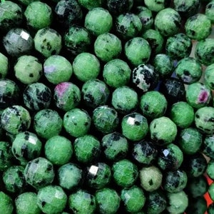 Puede incluir: Una hebra de cuentas de piedras preciosas verdes con motas negras y blancas. Las cuentas son facetadas y tienen forma redonda.