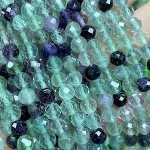 May include: A strand of green and purple faceted gemstone beads. The beads are round and have a smooth, polished finish.
