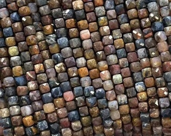May include: A strand of faceted gemstone beads in shades of brown, blue, and gold. The beads are square shaped and have a rough, natural texture.