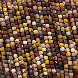 May include: A strand of multi-colored gemstone beads. The beads are small and square-shaped, with a faceted finish. The colors are a mix of red, brown, yellow, and white.