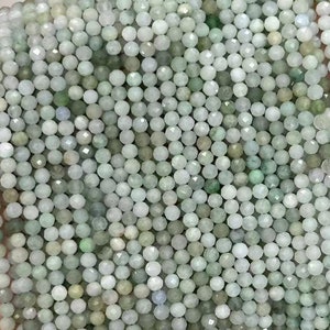 Puede incluir: Una hebra de cuentas de piedras preciosas facetadas de color verde claro. Las cuentas son pequeñas y redondas, y están enhebradas en un hilo transparente. Las cuentas están dispuestas en un patrón suelto y fluido.