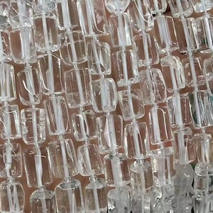 May include: A strand of clear quartz crystal beads, each bead is faceted and has a rectangular shape. The beads are strung on a clear thread and are approximately 10mm in size.