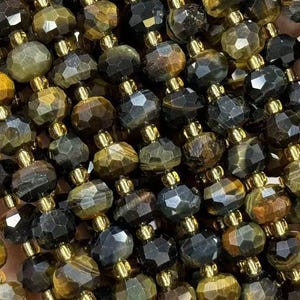 May include: Strands of faceted tiger eye gemstone beads in shades of brown, gold, and black. The beads are strung together with small gold-colored spacers. The gemstones have a polished, reflective surface, and are held in a hand.