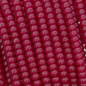 Może przedstawiać: Szereg głębokich czerwonych koralików z kamieni szlachetnych, każdy koralik jest okrągły i gładki. Koraliki są nawleczone na sznurek, tworząc długą naszyjnik lub bransoletkę.