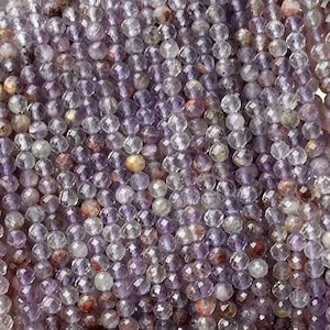 Pode incluir: Um fio de contas de pedras preciosas facetadas de cor púrpura e transparente. As contas são pequenas e redondas, e são enfiadas em um fio transparente. As contas são dispostas em um padrão aleatório, e criam um visual bonito e único.