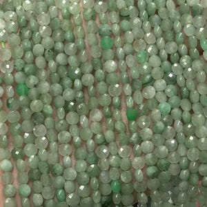 May include: Strands of small, faceted, light green beads. The beads are held in a hand, showcasing their color and texture. The beads appear to be strung together, ready for jewelry making or other crafts.
