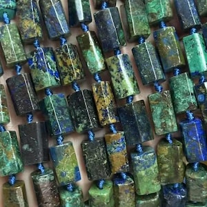 May include: Strands of natural gemstone beads in shades of blue, green, and brown. The beads are rectangular with faceted edges and strung on blue cord. The gemstones have a mottled appearance, with variations in color and texture. Ideal for jewelry making.
