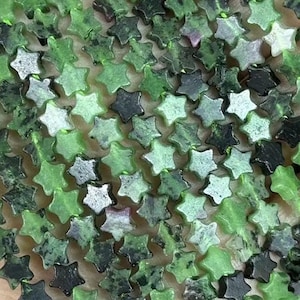 Könnte beinhalten: Eine Strähne grüner, sternförmiger Edelsteinperlen. Die Perlen sind grün marmoriert mit schwarzen und weißen Flecken.