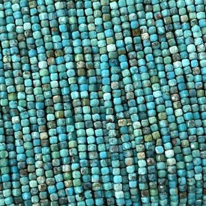 May include: Strands of turquoise-colored, square-cut beads. The beads are a mix of light and dark blue-green hues, creating a textured appearance. The beads are held in a hand, showcasing their color and shape. Ideal for jewelry making.