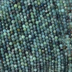 Puede incluir: Una hebra de cuentas de piedras preciosas facetadas de color azul verdoso. Las cuentas son pequeñas y de tamaño uniforme, y están enhebradas en un hilo transparente. Las cuentas tienen un ligero brillo iridiscente.